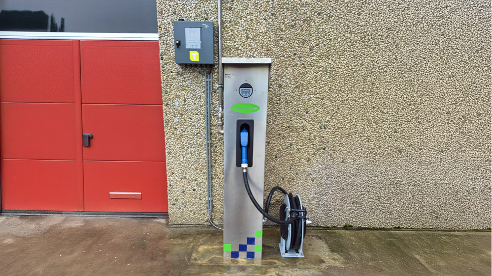 Elektrische laadpaal naast rode garagedeur